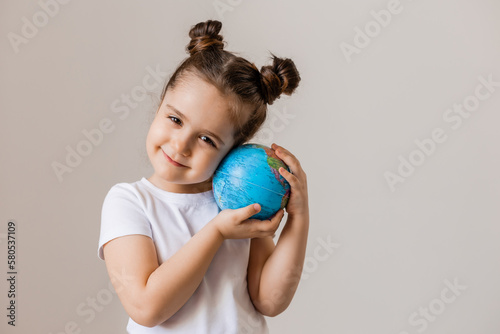 a happy little girl is holding a small globe planet in her hands in a white T-shirt on a white background. Earth Day, space for text