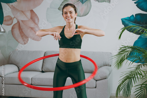 Young fun strong sporty athletic fitness trainer instructor woman wears green tracksuit hold using hula hoop for slim waist training do exercises at home gym indoor. Workout sport motivation concept