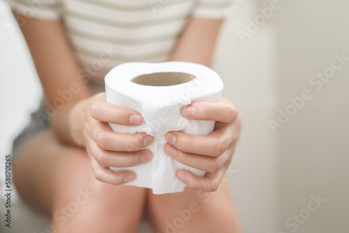 portrait of a woman suffers from diarrhea his stomach painful. ache and problem. hand hold tissue paper roll in front of toilet bowl. constipation in bathroom. Hygiene, health care concept.