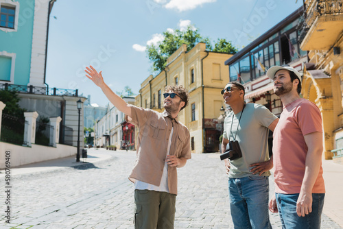 tour guide in sunglasses pointing with hand during excursion with interracial tourists on Andrews descent in Kyiv.