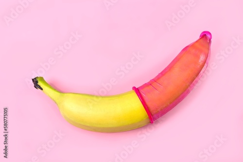 Red condom on banana with pink background. Safe sex concept. 