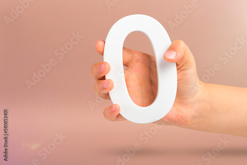 Numeral zero in hand. A hand holds a white number zero on a red background with copy space. Zero concept, 0 percent interest rate, minimum air emissions, cost or credit no increase.