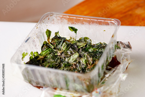 Spoiled mix of different salads in plastic packaging. Expired shelf life of fresh greens.