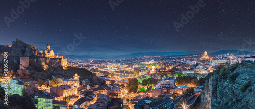Tbilisi, Georgia. Panorama Of Narikala Fortress, Sameba Holy Trinity Cathedral, Old Historic District Abanotubani In Night Illumination Under Amazing Blue Bright Night Starry Sky.