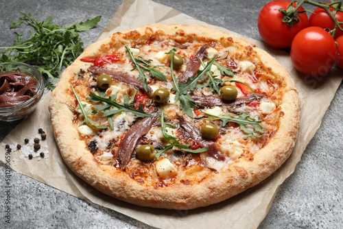 Tasty pizza with anchovies and ingredients on grey table