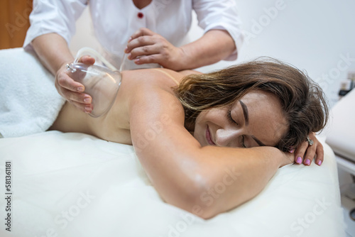 Body care procedure of a young female client lying on white sheets.