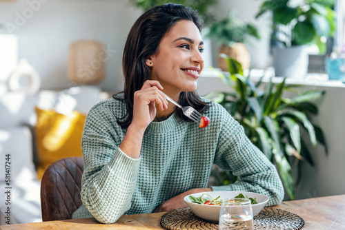 Beautiful smiling woman eating healthy salad at home.