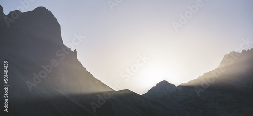 Minimalistic mountain landscape, the sun's rays shine from behind the mountain, a dark mountain at sunset in the evening, a panorama of minimalism in the mountains