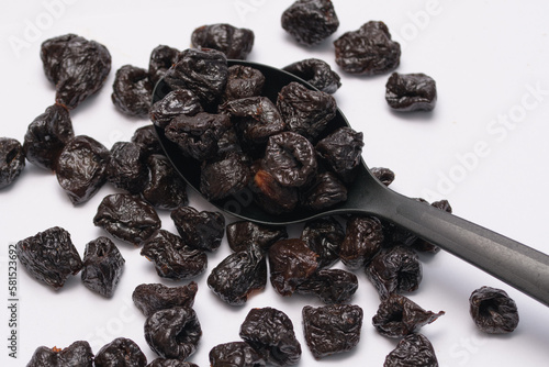 Suszone śliwki kalifornijskie leżące na czarnej łyżce kuchennej ba białym tle 
