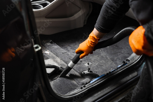 Vacuum cleaning of dirty car floor with removed seats in detailing service. Worker of detailing service is using vacuum cleaner for remove dust and dirt in car.