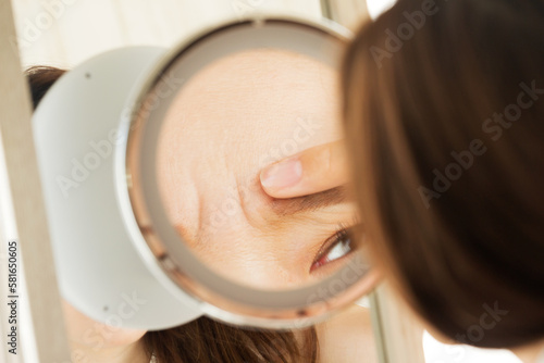 鏡で眉間のしわを見る女性。