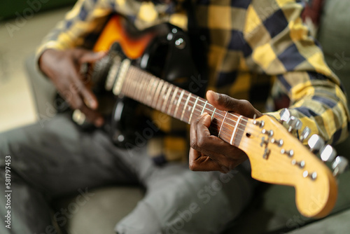 Young joyful african american man playing guitar in living room. Happy man enjoy at home.