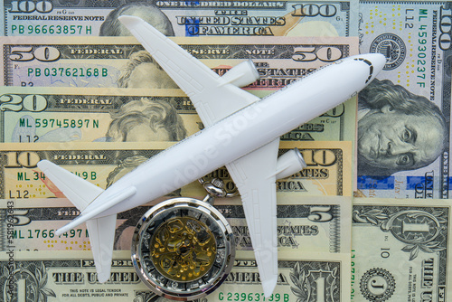Passenger plane and pocket watch sitting on US currency bills of different denominations showing concept high cost of flying, time 