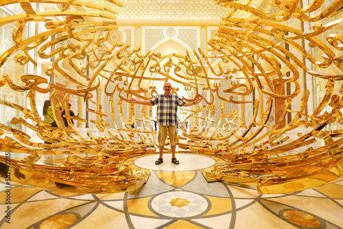 älterer aktiver Mann steht fröhlich im Präsidentenpalast in Abu Dhabi unter vergoldeter Dekoration des Eingangs