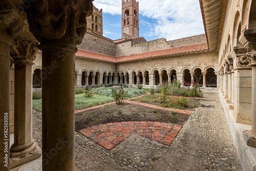 Courtyard of arched colonnaded Elne Cathedral with cobblestone paving and green plants