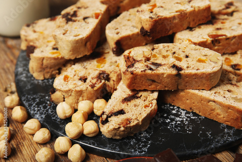 Board with delicious biscotti cookies and hazelnuts on wooden background