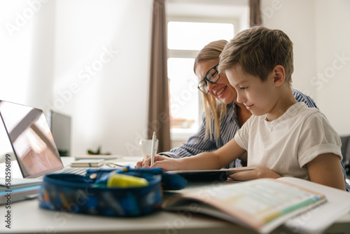 Happy mom and son doing homework and studying with laptop together. Home education