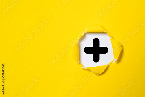 Black plus sign inside punch yellow paper for positive thinking mindset or healthcare insurance symbol or value added concept.
