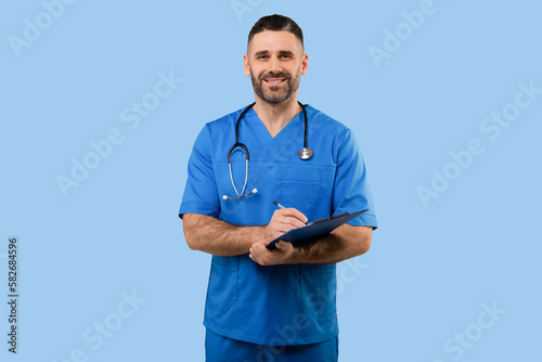 Middle aged male doctor in uniform working with patient anamnesis, standing over blue background and smiling at camera