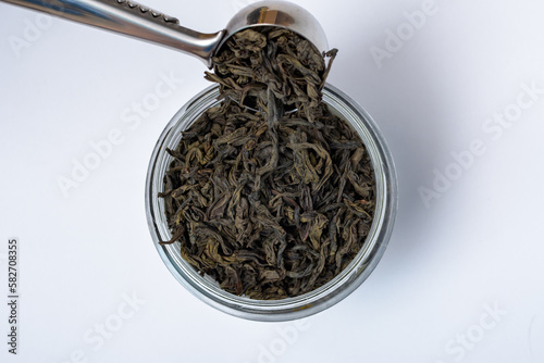 Czarna herbata lisciasta przesypywana z metalowej łyżeczki do słoika 