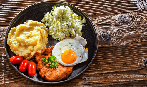 Breaded chicken cutlet with fried egg, potatoes and cabbage