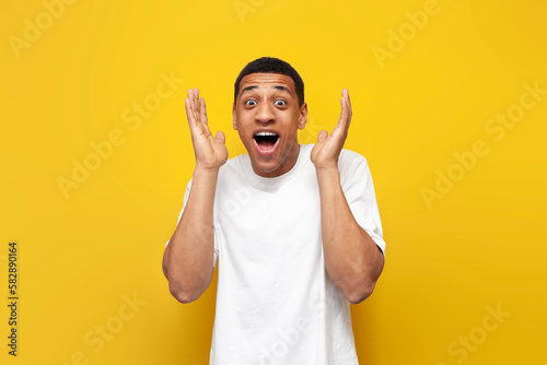 young surprised guy african american in white t-shirt raises his hands in front of him and opens his mouth