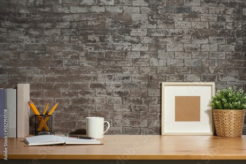 Blank picture frame, coffee cup, notebook and potted plant on wooden table. Stylish working space, home office.