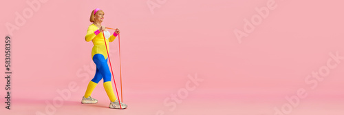 Senior old woman in colorful sportswear training with sport expanders, posing against pink studio background. Concept of sportive lifestyle, retirement, health care, wellness. Copy space for ad