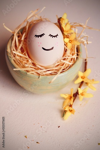 Wesoła pisanka na Wielkanoc - jajko z buźką w gniazdku. Symbol świąt wielkiej nocy i gałązka forsycji