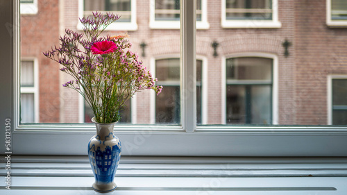 Pink and peach-colored Barberton daisy flower heads, Chamelaucium uncinatum or geraldton waxflower, and Salt Cedar or Tamarix ramosissima in a white Dutch vase in front of the white window ledge