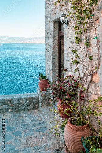 Terrace with outdoor decoration of terracotta pots against an ancient facade overlooking the Aegean Sea, Hydra Island, Greece.