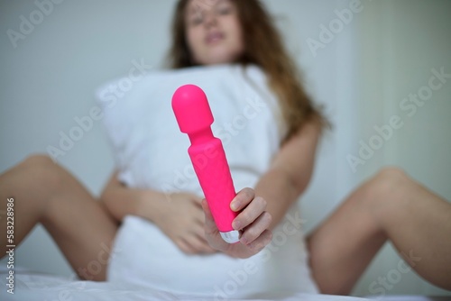 Young happy sexy woman hold in hand sex toy, masturbate with vibrator in bed in bedroom at home.