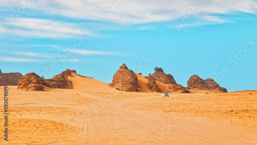 Typical desert landscape in Alula, Saudi Arabia, sand with some mountains, small offroad vehicle, local man and camels at distance