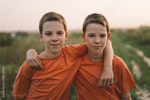 Funny twin brother boys in orange t-shirt playing outdoors on field at sunset. Happy children, lifestyle.