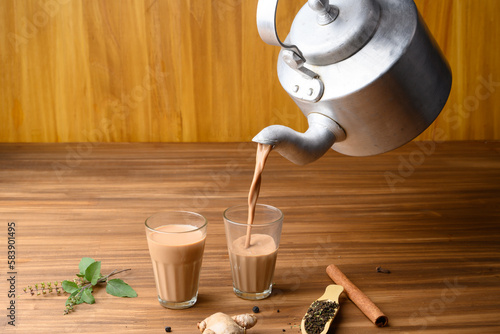 indian masala chai or tea in traditional glasses, with kettle, spices and tea leaves on dark, wooden background.