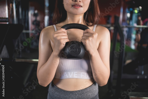 A young anonymous woman does a set of goblet squats with a kettlebell. Training at a modern gym.