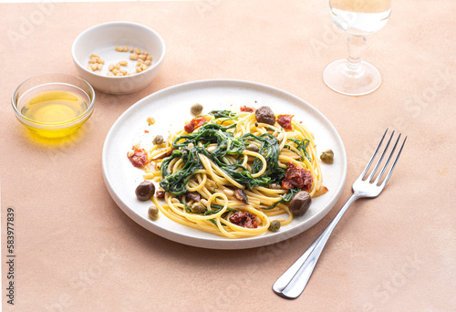 Spaghetti with Italian Agretti, Barba di frate or Saltwort or Salsola Soda, olives, anchovy, tomatoes, capers,  pine nuts and olive oil, spring Italian recipes. Pink soft spring background