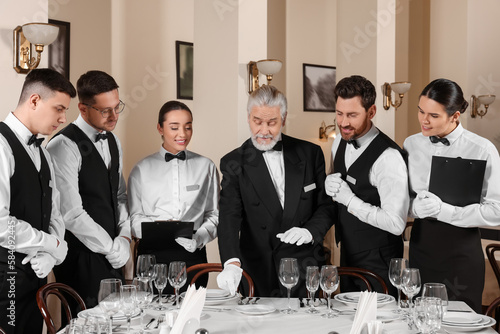 Senior man wearing formal suit teaching trainees in restaurant. Professional butler courses