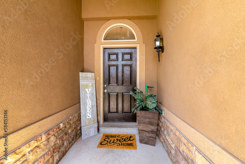 Horizontal shot of a house with black front door with arched transom window. Entrance in between the walls with and decorative panel with VIBES lettering on the left and potted plants on the right.