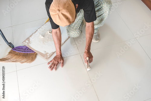 A handy man prepares the edge of floor tiles for the application of new grout to fill the gaps. Home renovation or finishing works.