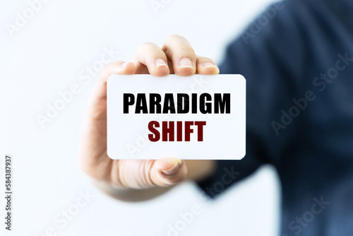 Paradigm shift text on blank business card being held by a woman's hand with blurred background. Business concept about paradigm shift.