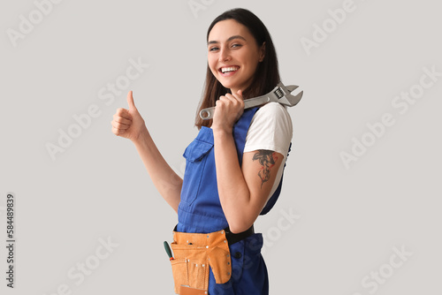 Female plumber with wrench showing thumb-up on grey background