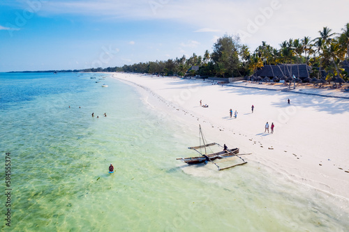 Take in the stunning scenery of Zanzibar's tropical coast from above, as fishing boats rest on the sandy beach at sunrise. The view from the top reveals clear blue waters, green palm trees, and even 