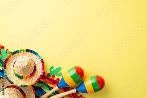 Cinco de Mayo celebration concept. Top flat lay photo of mexican sombrero colorful poncho maracas cactus decoration isolated on pastel yellow background with copy space