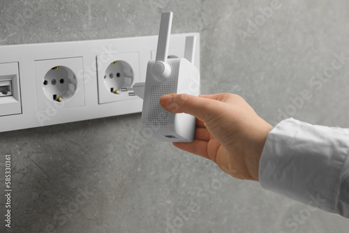 Woman inserting wireless Wi-Fi repeater into power socket indoors, closeup