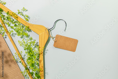 Sustainable, ecological shopping, buying or sales concept. Eco friendly still life with wooden hanger with green branches and empty label on blue background with plant shadows. Flat lay, copy space