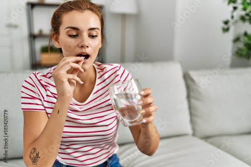 Young woman taking pills sitting on sofa at home