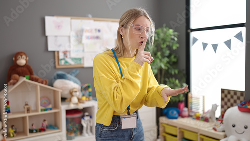 Young blonde woman preschool teacher asking for silence at kindergarten