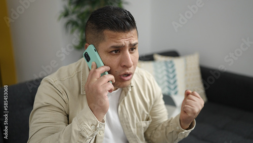 Young hispanic man speaking on the phone complaining at home