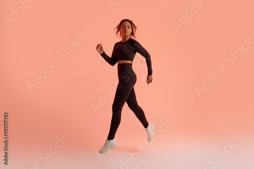 Black female athlete jumping, running, exercising during training over neon studio background, full length